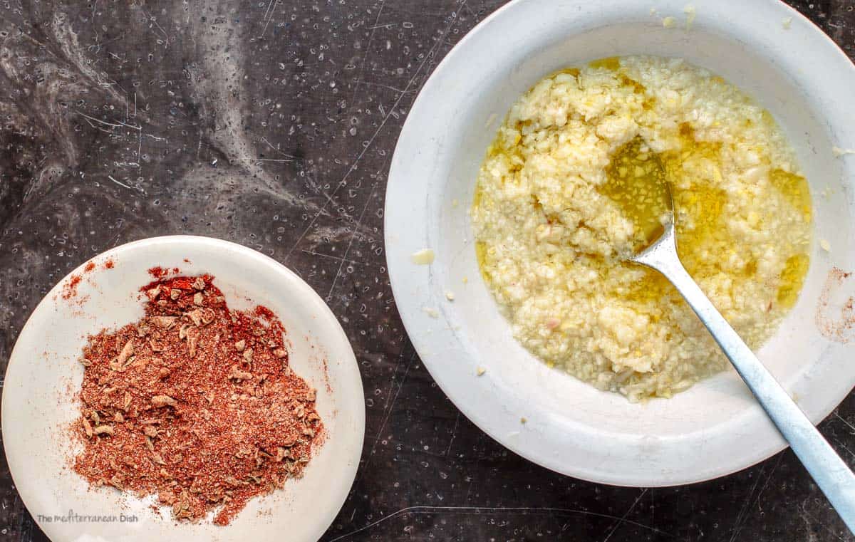 Minced garlic and seasoning for chicken kabob marinade in bowls.