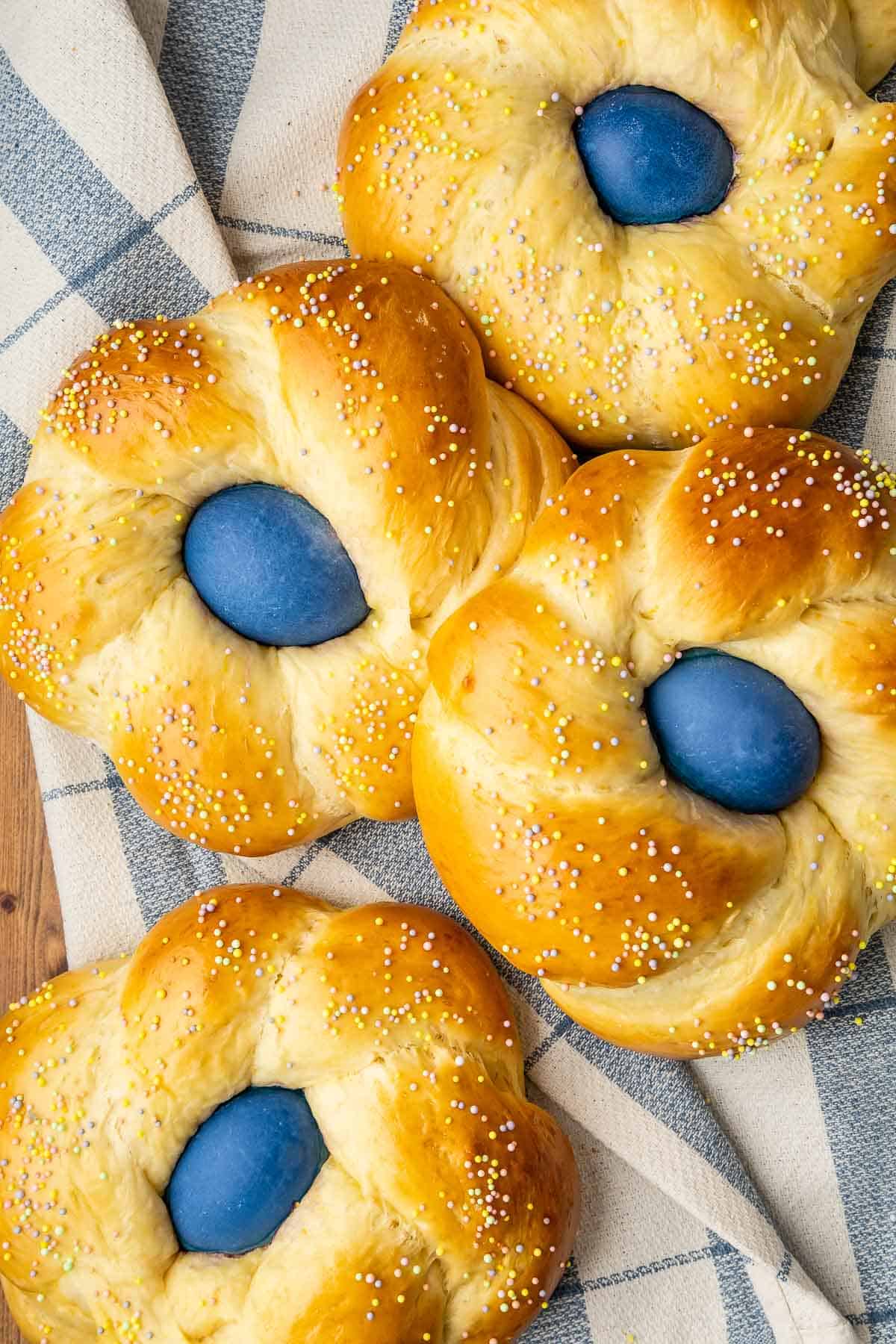 Four braised nests of Italian Easter Breads with a naturally dyed blue egg in the center and colored sprinkles.