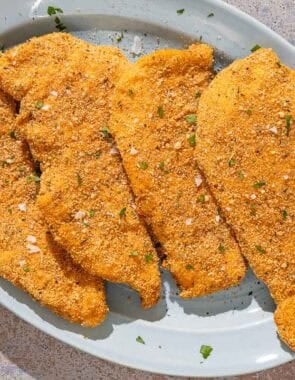 Four parmesan crusted chicken fillets on a platter.