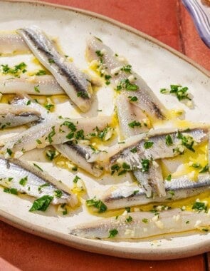 Boquerones on a platter next to a bowl of green olives.