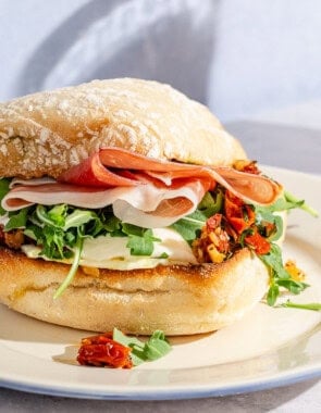 A breakfast sandwich on a plate next to a glass of orange juice.