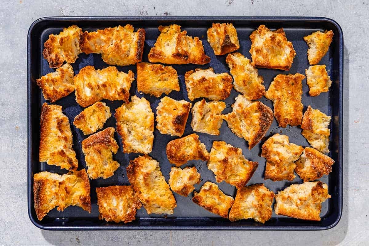 The torn pieces of crusty bread for the burrata salad toasted on a sheet pan.