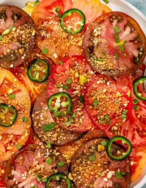 Heirloom tomato salad topped with dukkah and mint on a platter with a spoon next to a cup of the dressing and a small bowl of dukkah.