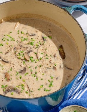 Mushroom soup in a large pot. Next to this is a stack of bowls with 2 spoons, and a small bowl of chopped chives.