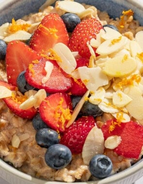 Oatmeal topped with strawberries, blueberries, chia seeds, almonds and orange zest in a bowl with a spoon.