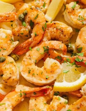 A close up of shrimp piccata with lemon wedges.