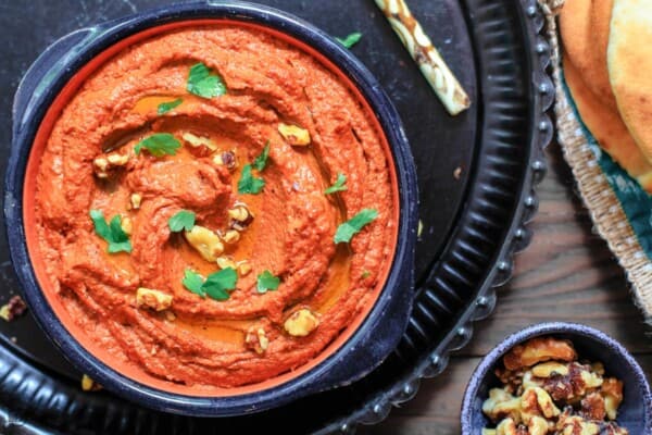 Muhammara dip in a bowl. A side of walnuts and pita
