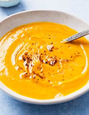 A close up of pumpkin soup topped with the Aleppo pepper-garlic oil in a bowl with a spoon.