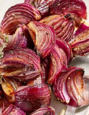 Roasted red onions on a platter with a serving spoon.