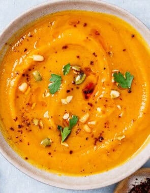 An overhead photo of a bowl of butternut squash apple soup next to a bowl of aleppo pepper.