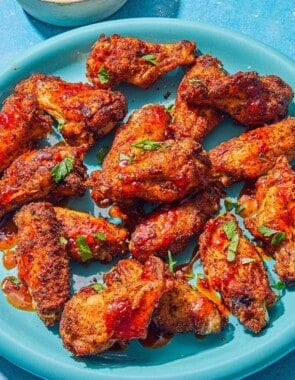 Air fryer chicken wings topped with harissa hot honey and chopped parsley on a platter. Next to this is a bowl of creamy feta dressing.