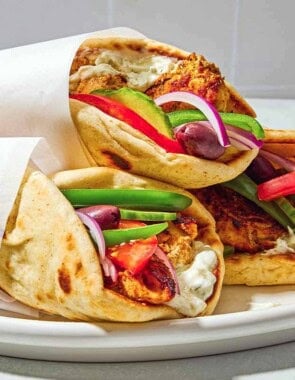 Three chicken gyros on a plate, each one wrapped in parchment paper.