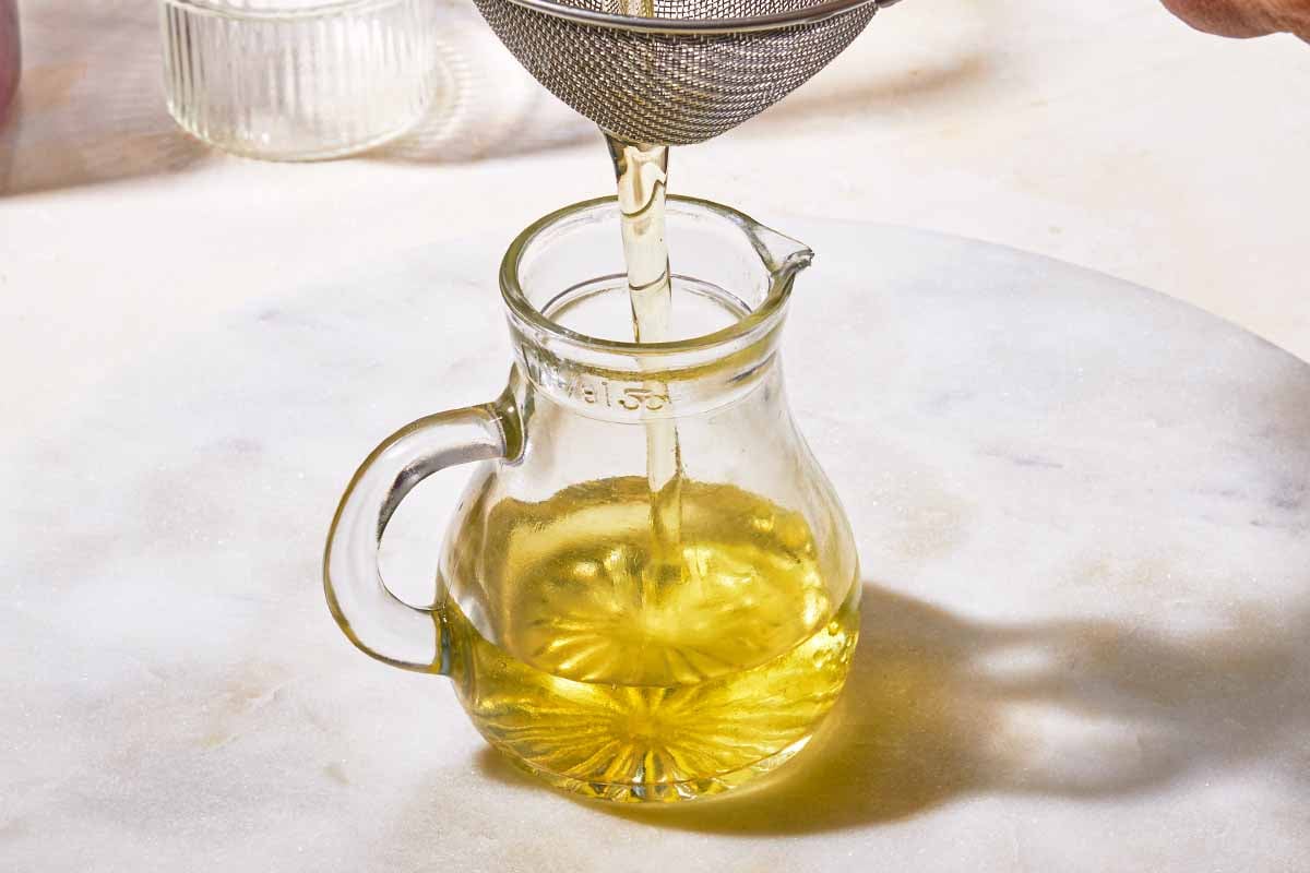 The simple syrup for the cranberry mocktail being poured through a strainer into a small bottle.