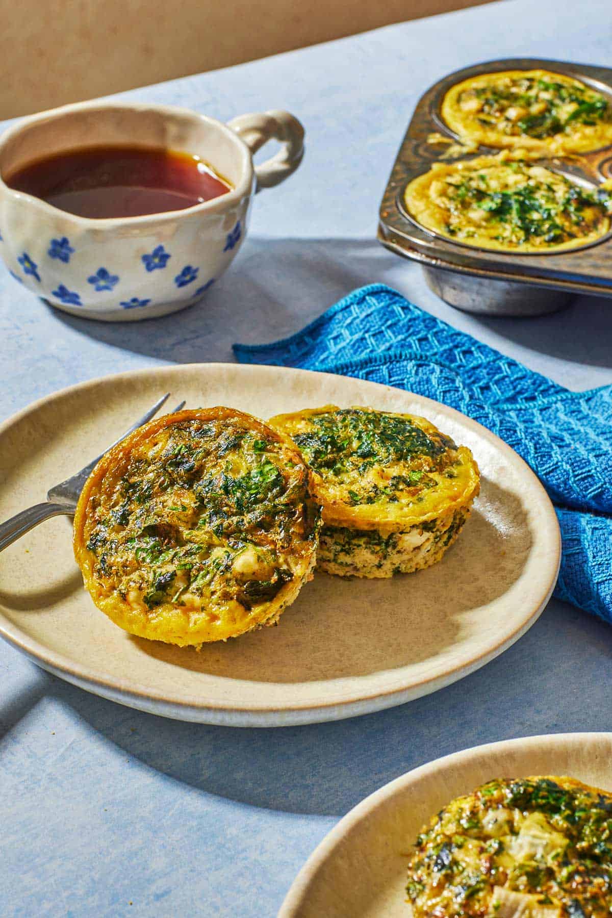 Golden-brown Spanakopita egg muffins with visible spinach and feta, served on a ceramic plate for a Mediterranean breakfast.