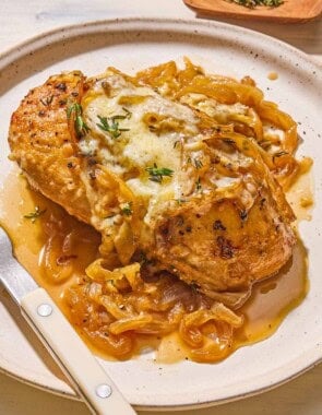 A serving of french onion chicken on a plate with a fork. Next to this is a bowl of chopped thyme.