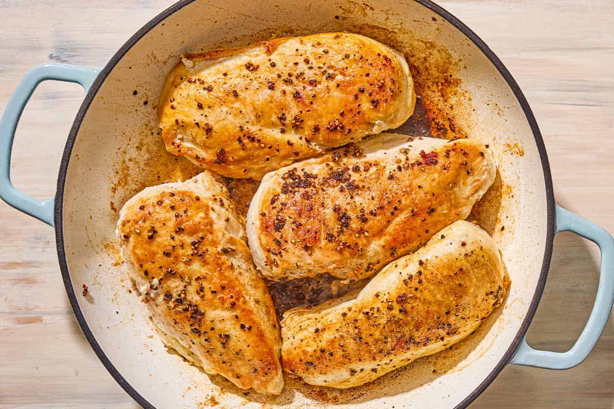 Four chicken breast fillets being browned in a skillet.