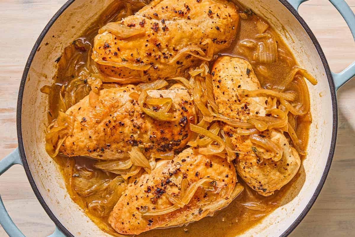The browned chicken nestled into the sauteed onions and dripping in a skillet