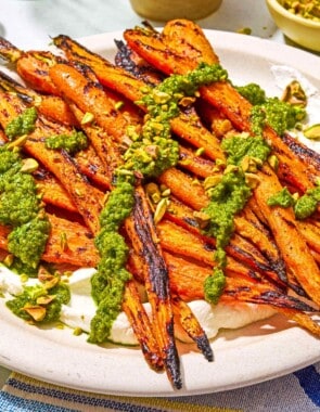 Grilled carrots with labneh topped with zhoug and chopped pistachios on a platter.