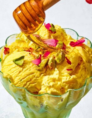 A goblet with persian ice cream being drizzled with honey from a honey dipper.