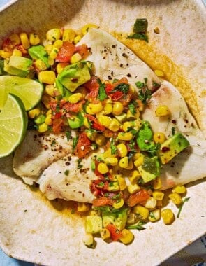 Poached flounder topped with sweet corn salsa on a plate with lime wedges.