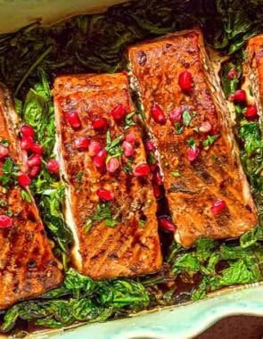 Glazed salmon fillets topped with pomegranate arils on a bed of baby spinach in a baking dish.