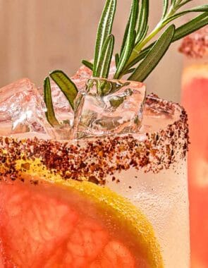 A close up of a glass of the rosemary grapefruit tonic with a grapefruit wheel, a sprig of rosemary and a sumac rim.