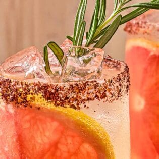 A close up of a glass of the rosemary grapefruit tonic with a grapefruit wheel, a sprig of rosemary and a sumac rim.