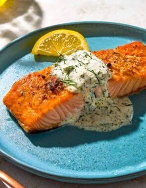 A serving of lemon dill salmon on a plate with a lemon wedge.