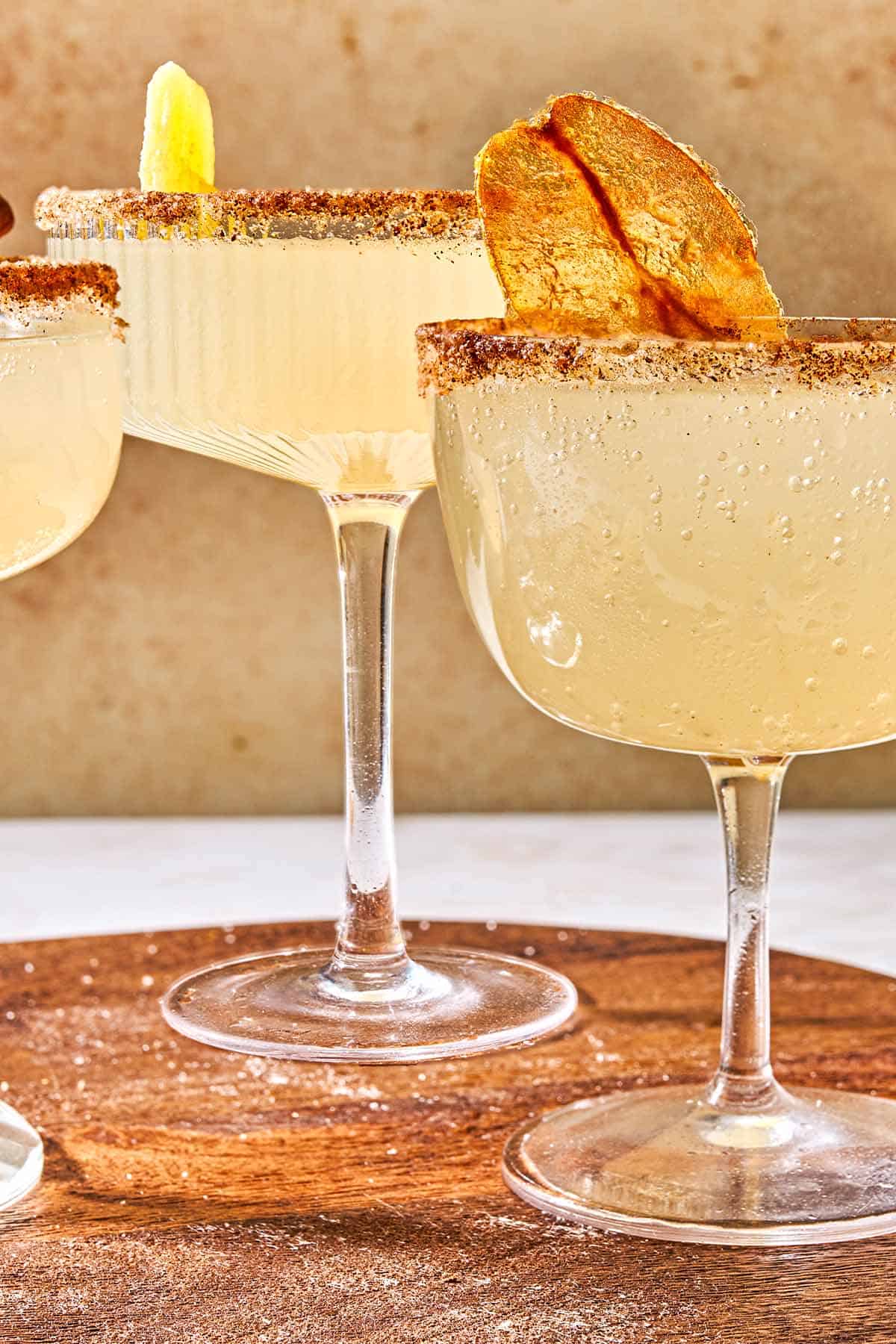 A close up of two ginger beer mocktails on a wooden tray. On is garnished with a candied pear chip and other with a crystalized ginger slice.