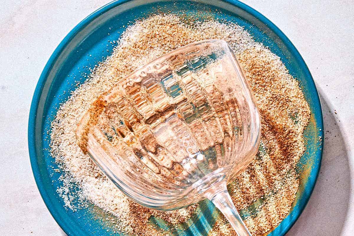 The rim of a glass for the ginger beer mocktail being rolled in a bowl of sugar, cinnamon and cardamom.
