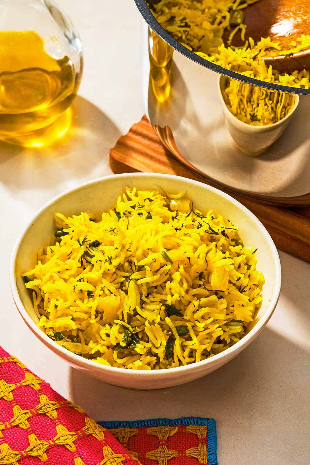 A bowl of turmeric rice next to the rest of the rice in a bowl and a bottle of olive oil.
