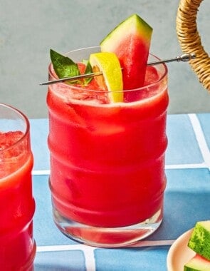 A glass of watermelon lemonade garnished with basil and slices of watermelon and lemon.