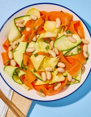 Zucchini ribbon salad in a bowl next to a cloth napkin, and a wooden spoon.